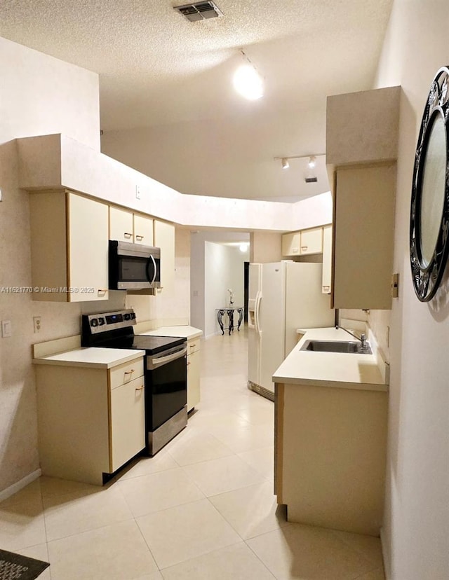 kitchen with appliances with stainless steel finishes, a textured ceiling, sink, cream cabinetry, and light tile patterned flooring