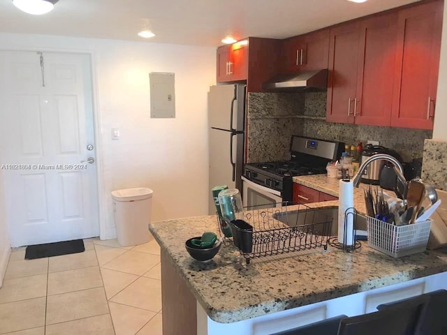 kitchen featuring electric panel, freestanding refrigerator, a peninsula, stainless steel gas range, and under cabinet range hood