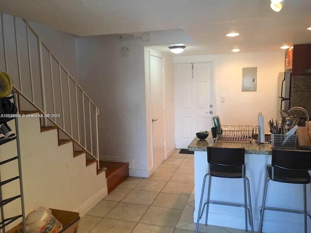 kitchen with light tile patterned floors, dark countertops, freestanding refrigerator, a peninsula, and a kitchen bar