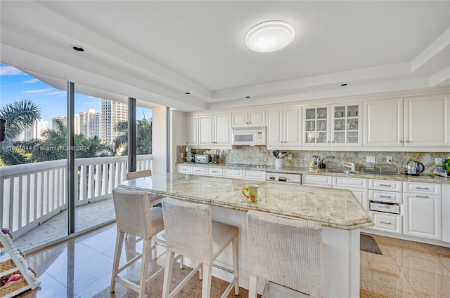 kitchen with decorative backsplash, light stone counters, white cabinets, and white appliances