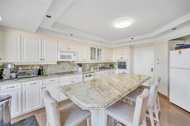 kitchen with a raised ceiling, light stone countertops, a center island, and white appliances