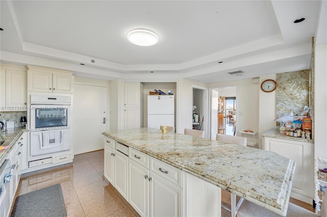 kitchen with a center island, a raised ceiling, light stone counters, white fridge, and a breakfast bar area