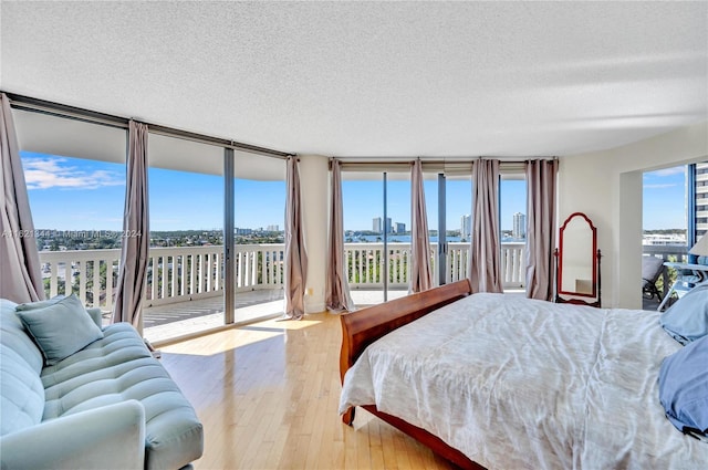 bedroom with access to outside, floor to ceiling windows, a textured ceiling, and light wood-type flooring