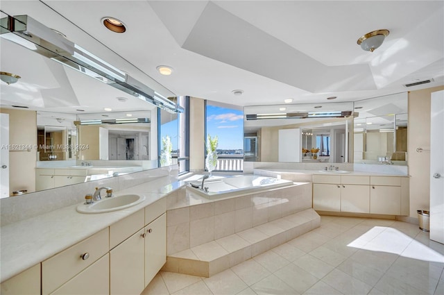 bathroom with tile patterned flooring, vanity, a raised ceiling, and tiled bath