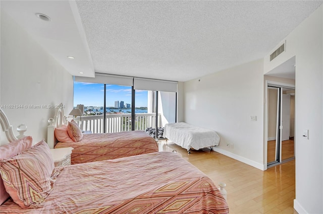 bedroom with floor to ceiling windows, light wood-type flooring, a textured ceiling, and access to outside