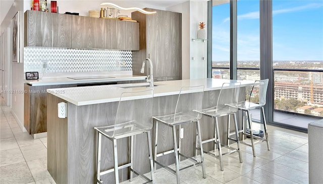 kitchen with sink, backsplash, a kitchen breakfast bar, a wall of windows, and a center island with sink