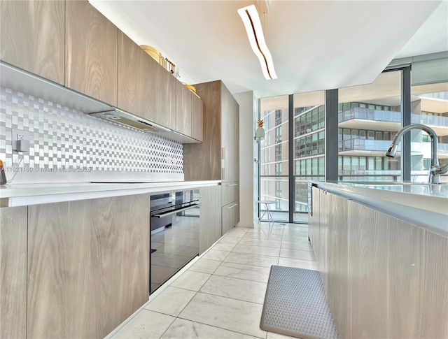 kitchen featuring light tile patterned flooring, sink, black oven, and backsplash