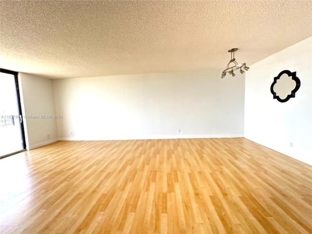 empty room with an inviting chandelier, a textured ceiling, and light wood-type flooring