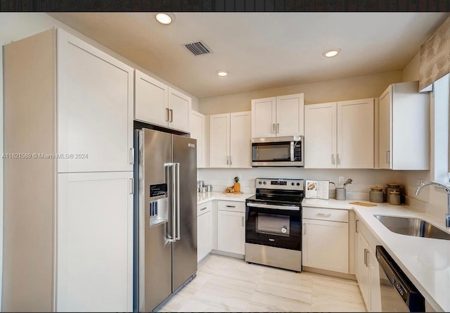 kitchen with sink, white cabinets, light tile patterned floors, and stainless steel appliances