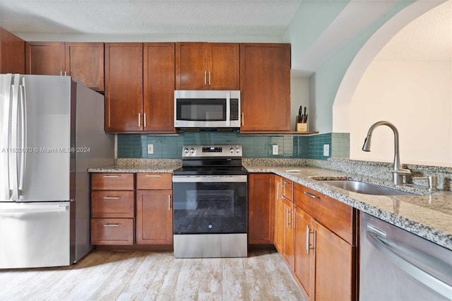 kitchen featuring stainless steel appliances, sink, light stone counters, light hardwood / wood-style floors, and backsplash