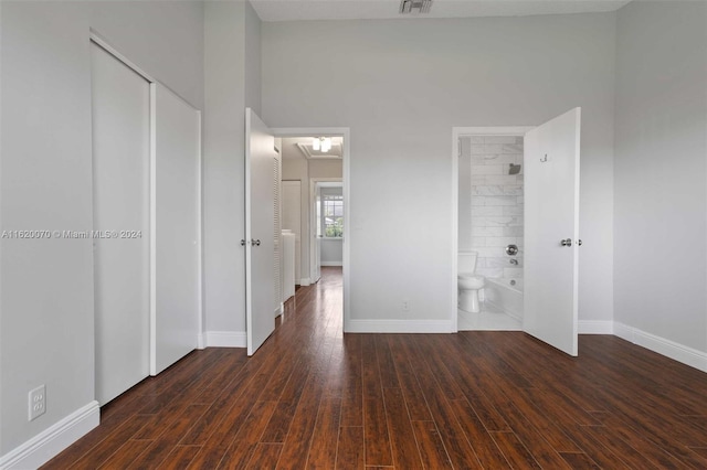 unfurnished bedroom with dark hardwood / wood-style floors, ensuite bath, and a high ceiling