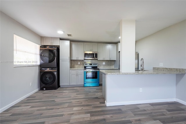 kitchen featuring stainless steel appliances, stacked washer / dryer, light stone counters, and kitchen peninsula