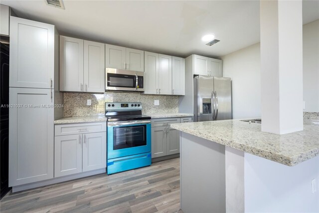 kitchen with appliances with stainless steel finishes, light hardwood / wood-style flooring, kitchen peninsula, decorative backsplash, and light stone countertops