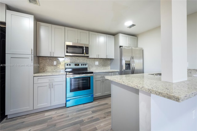 kitchen featuring light stone countertops, appliances with stainless steel finishes, light wood-type flooring, and decorative backsplash