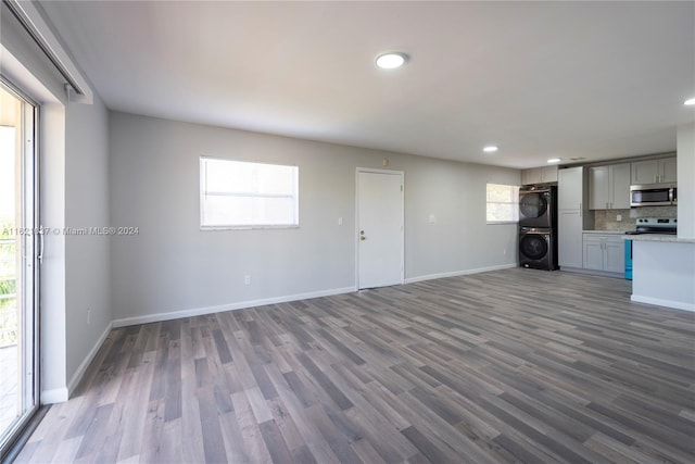 unfurnished living room featuring dark hardwood / wood-style flooring, stacked washer and dryer, and a healthy amount of sunlight