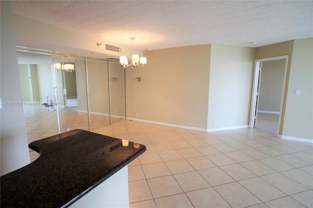 unfurnished room with a chandelier, light tile patterned floors, and a textured ceiling