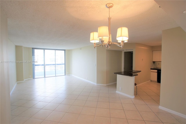 empty room featuring a chandelier, light tile patterned floors, a textured ceiling, and a wall of windows