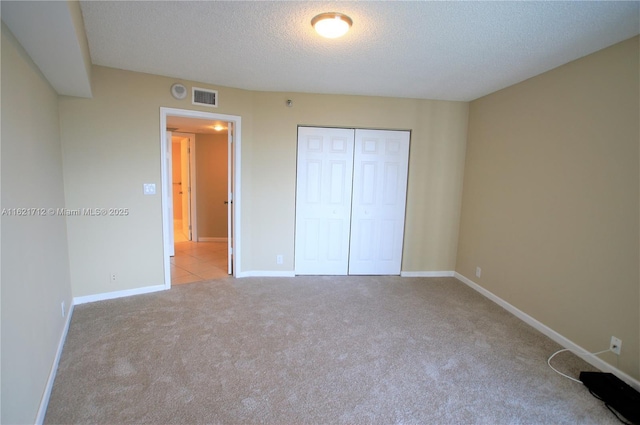 unfurnished bedroom featuring light carpet, a closet, and a textured ceiling