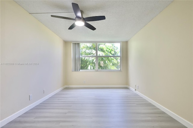 empty room with ceiling fan, light wood-type flooring, and a textured ceiling