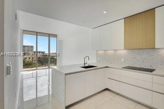 kitchen featuring kitchen peninsula, decorative backsplash, sink, white cabinetry, and light tile patterned floors