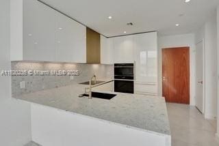 kitchen featuring white cabinets, sink, backsplash, kitchen peninsula, and light stone counters