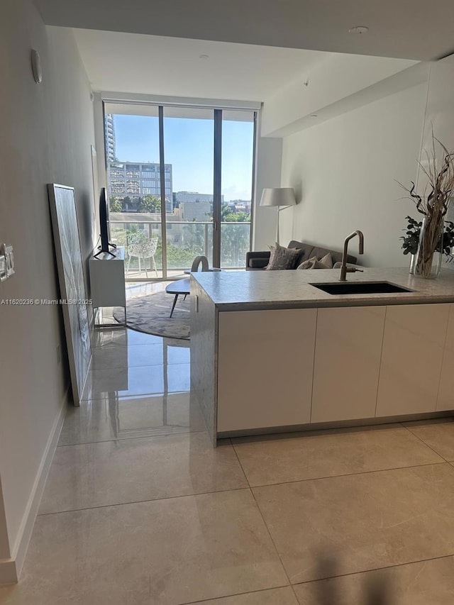 2678 Tigertail Ave Unit 515, Miami, FL 33133 - kitchen with floor to ceiling windows, a sink, baseboards, light tile patterned floors, and white cabinets
