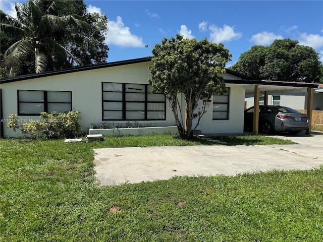 back of house with stucco siding, concrete driveway, a lawn, and an attached carport