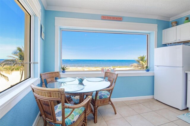 dining space featuring a water view, a textured ceiling, light tile patterned floors, and crown molding