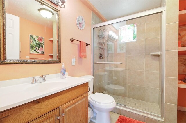 bathroom featuring tile patterned flooring, a shower with door, toilet, and vanity