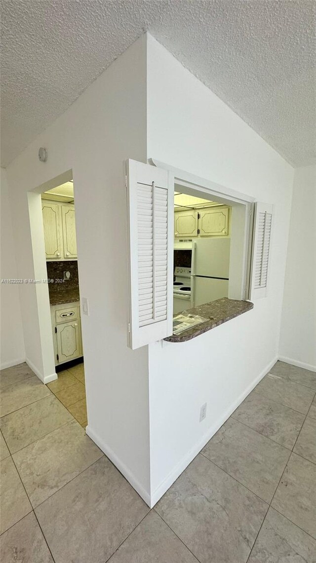 interior space with light tile patterned flooring, a textured ceiling, tasteful backsplash, and white appliances