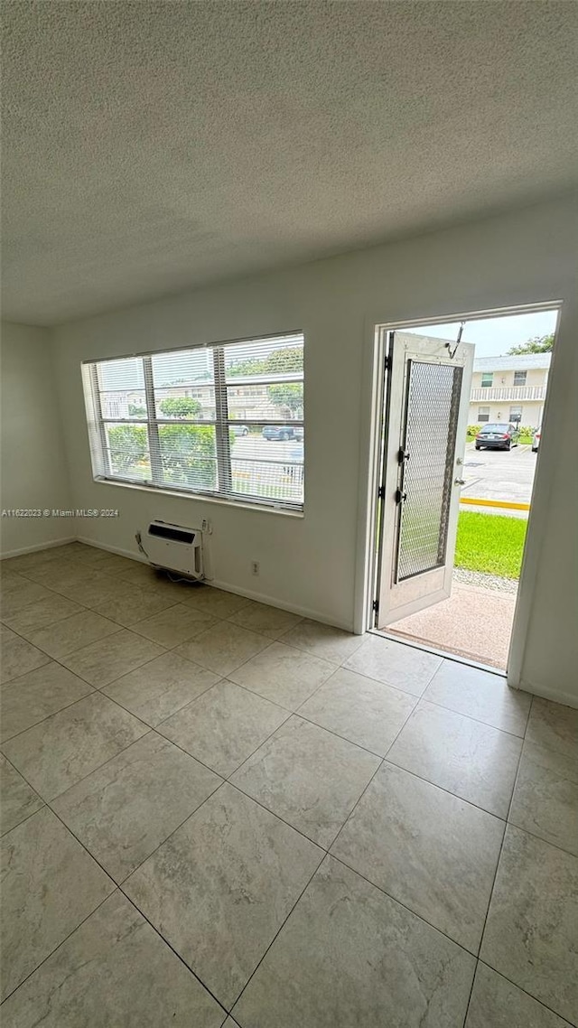 unfurnished room with light tile patterned flooring, a wall mounted AC, and a textured ceiling