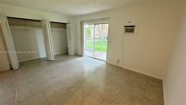 unfurnished bedroom featuring a textured ceiling, two closets, access to exterior, and a wall unit AC