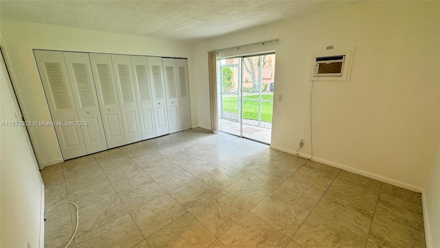 unfurnished bedroom featuring an AC wall unit, access to outside, a closet, and a textured ceiling