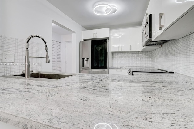 kitchen with stainless steel fridge, white cabinets, tasteful backsplash, black stove, and sink