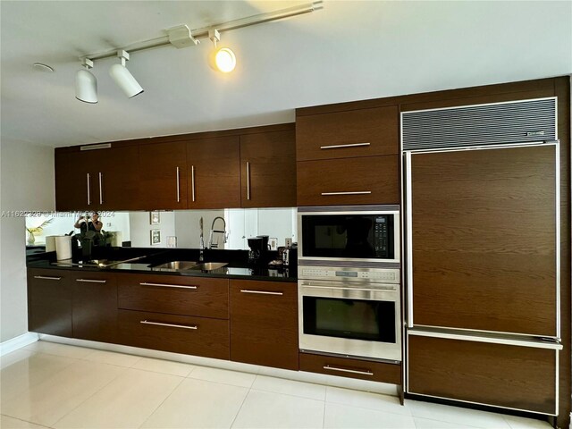 kitchen featuring light tile patterned flooring, track lighting, sink, and built in appliances