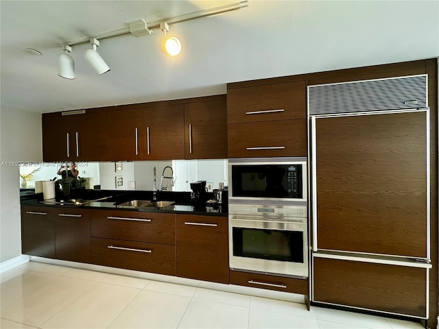 kitchen featuring built in appliances, sink, dark brown cabinets, and light tile patterned floors