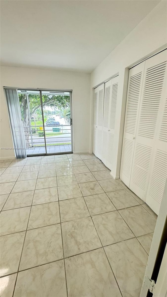 unfurnished bedroom with light tile patterned floors, access to exterior, and two closets