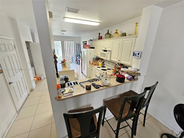 kitchen with light tile patterned floors, cream cabinetry, a textured ceiling, and white appliances