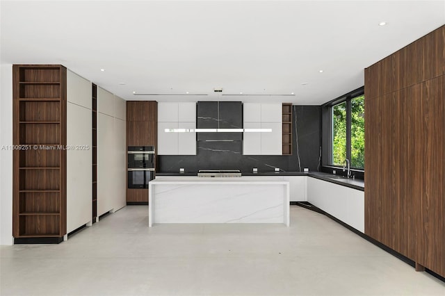 kitchen with white cabinetry, backsplash, multiple ovens, light stone counters, and a kitchen island