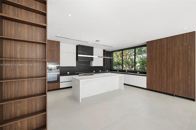 kitchen featuring a kitchen island, white cabinetry, sink, decorative backsplash, and stainless steel oven