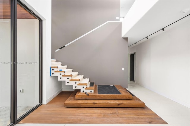 stairs with a towering ceiling, wood-type flooring, and rail lighting