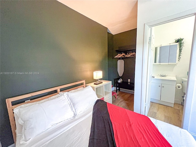 bedroom with vaulted ceiling, light wood-type flooring, ensuite bathroom, and sink