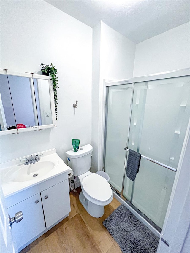 bathroom featuring a shower with shower door, hardwood / wood-style flooring, vanity, and toilet