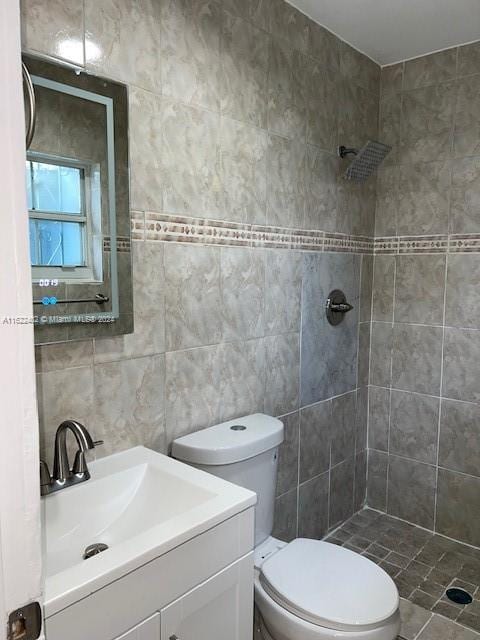 bathroom featuring vanity, tiled shower, tile walls, and toilet