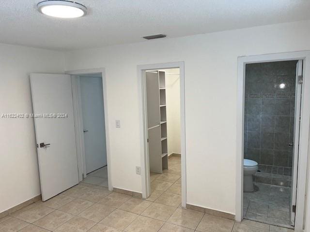 unfurnished bedroom with light tile patterned flooring, connected bathroom, and a walk in closet