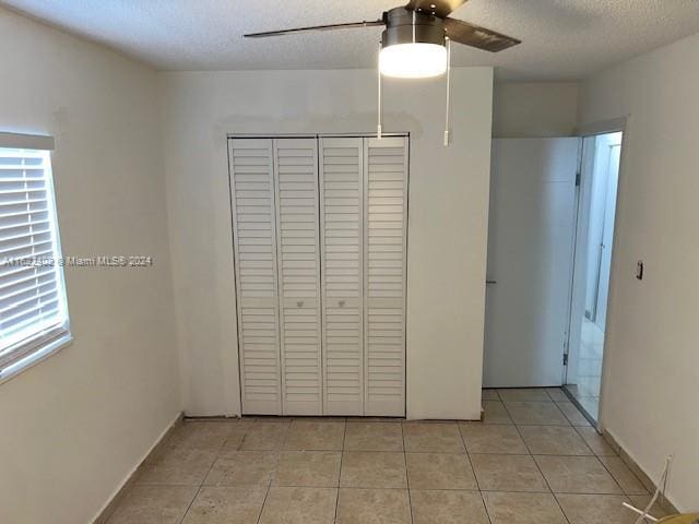 unfurnished bedroom with a closet, a textured ceiling, light tile patterned floors, and ceiling fan