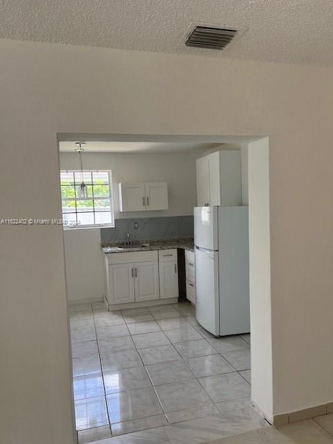 kitchen with white cabinets, white refrigerator, sink, light tile patterned floors, and a textured ceiling