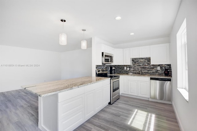 kitchen with light hardwood / wood-style flooring, stainless steel appliances, light stone counters, pendant lighting, and decorative backsplash