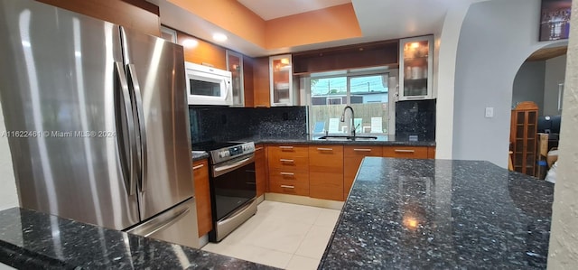 kitchen with dark stone counters, sink, appliances with stainless steel finishes, tasteful backsplash, and light tile patterned floors