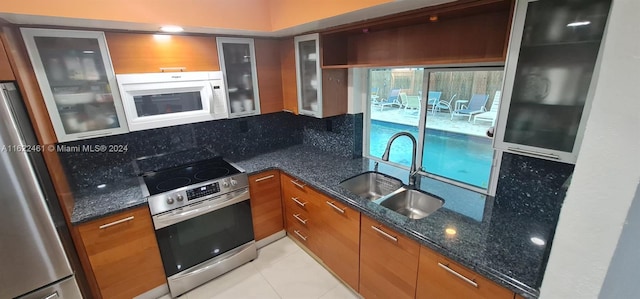 kitchen featuring stainless steel appliances, tasteful backsplash, sink, light tile patterned floors, and dark stone countertops